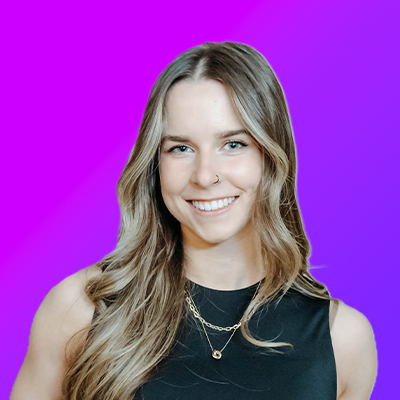 Smiling young man with glasses and dreadlocks wearing a light beige sweater against a bright blue gradient background.