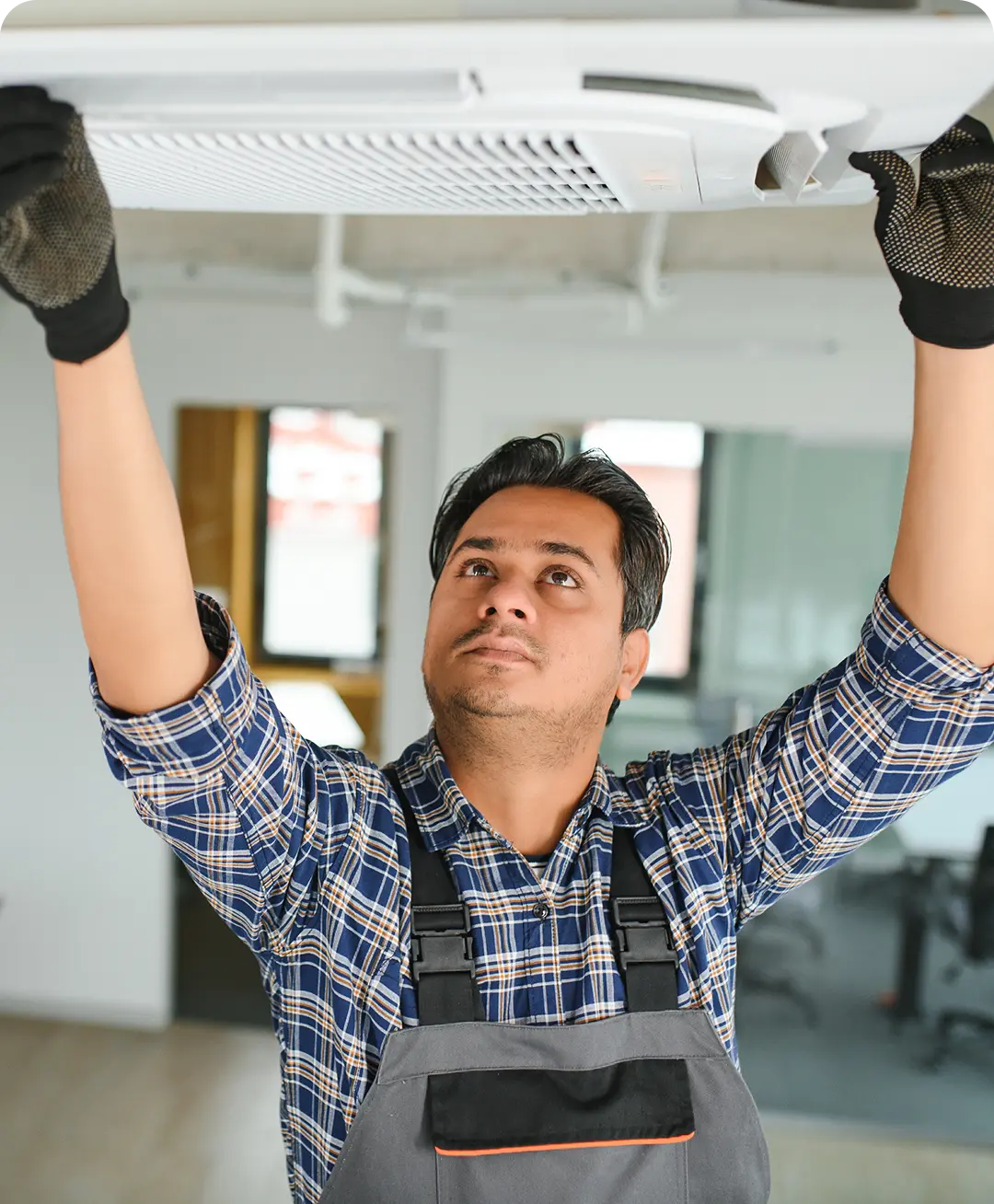 Man in plaid shirt and overalls inspecting or installing a white ceiling air conditioning unit indoors hired with uSource app