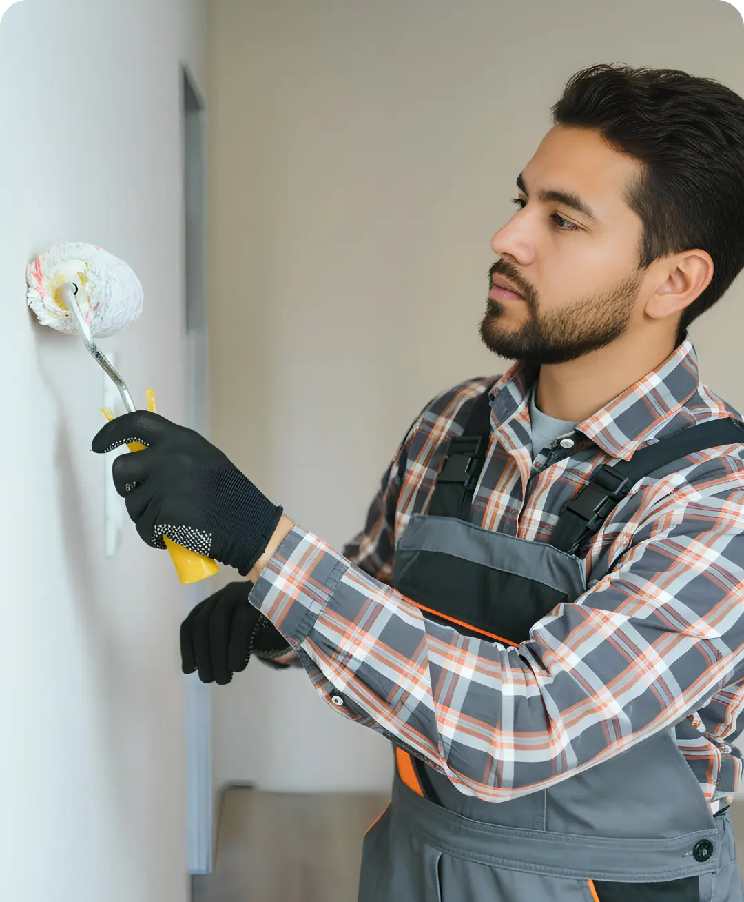 Man wearing gloves and overalls painting a white wall with a paint roller hired with uSource app