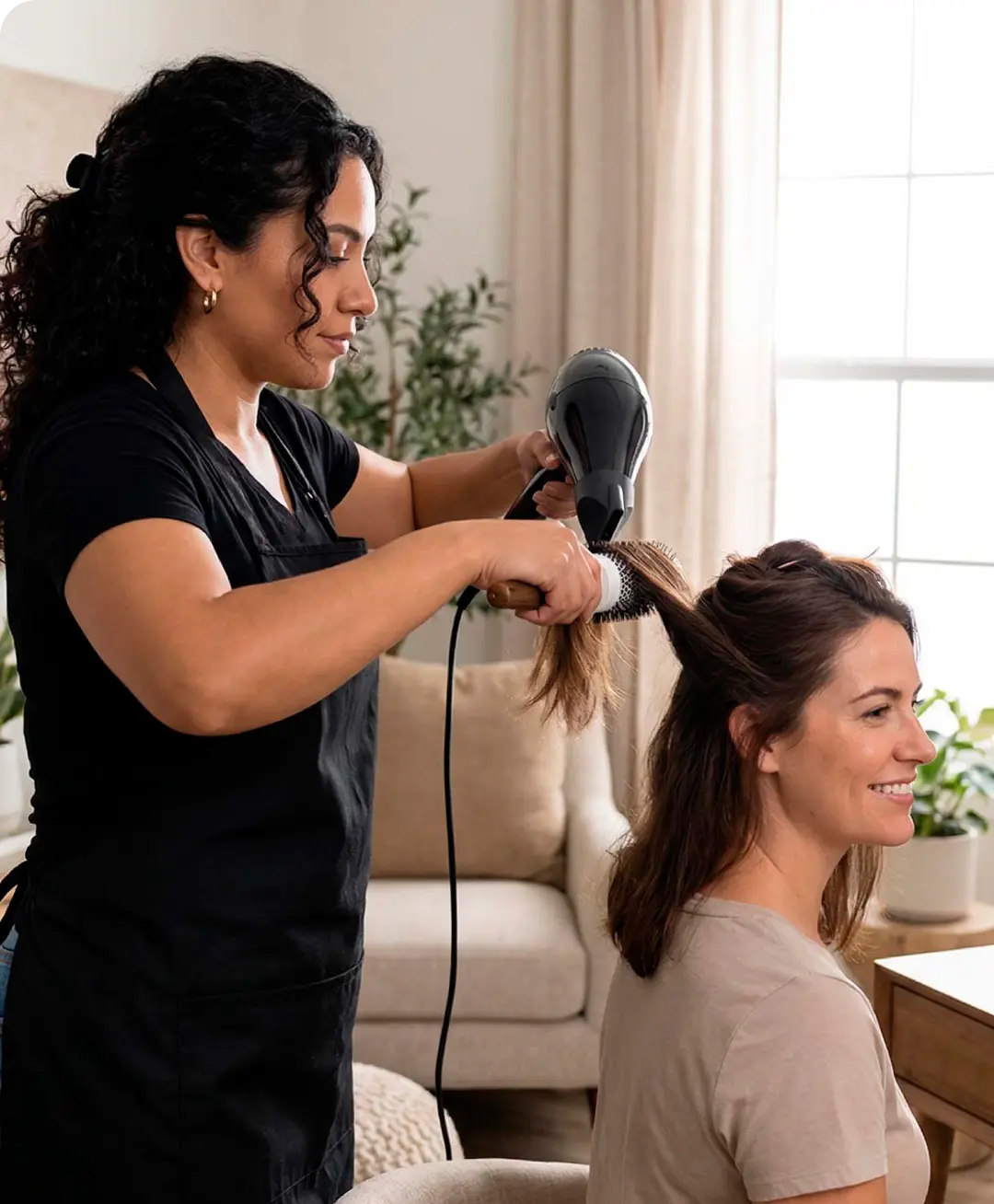 Hairdresser blow-drying a smiling woman's hair using a round brush in a bright, cozy room hired with uSource app