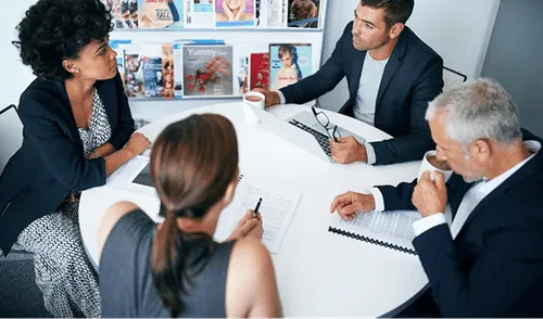 Four business professionals engaged in a meeting around a white table with documents and coffee cups.