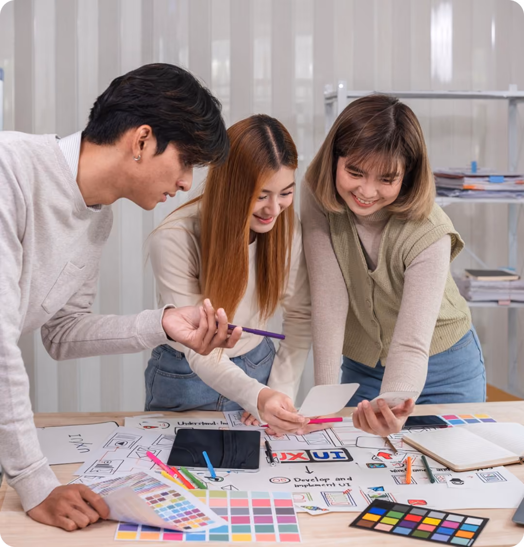 Three people collaborating on a design project with color swatches and sketches on a table.