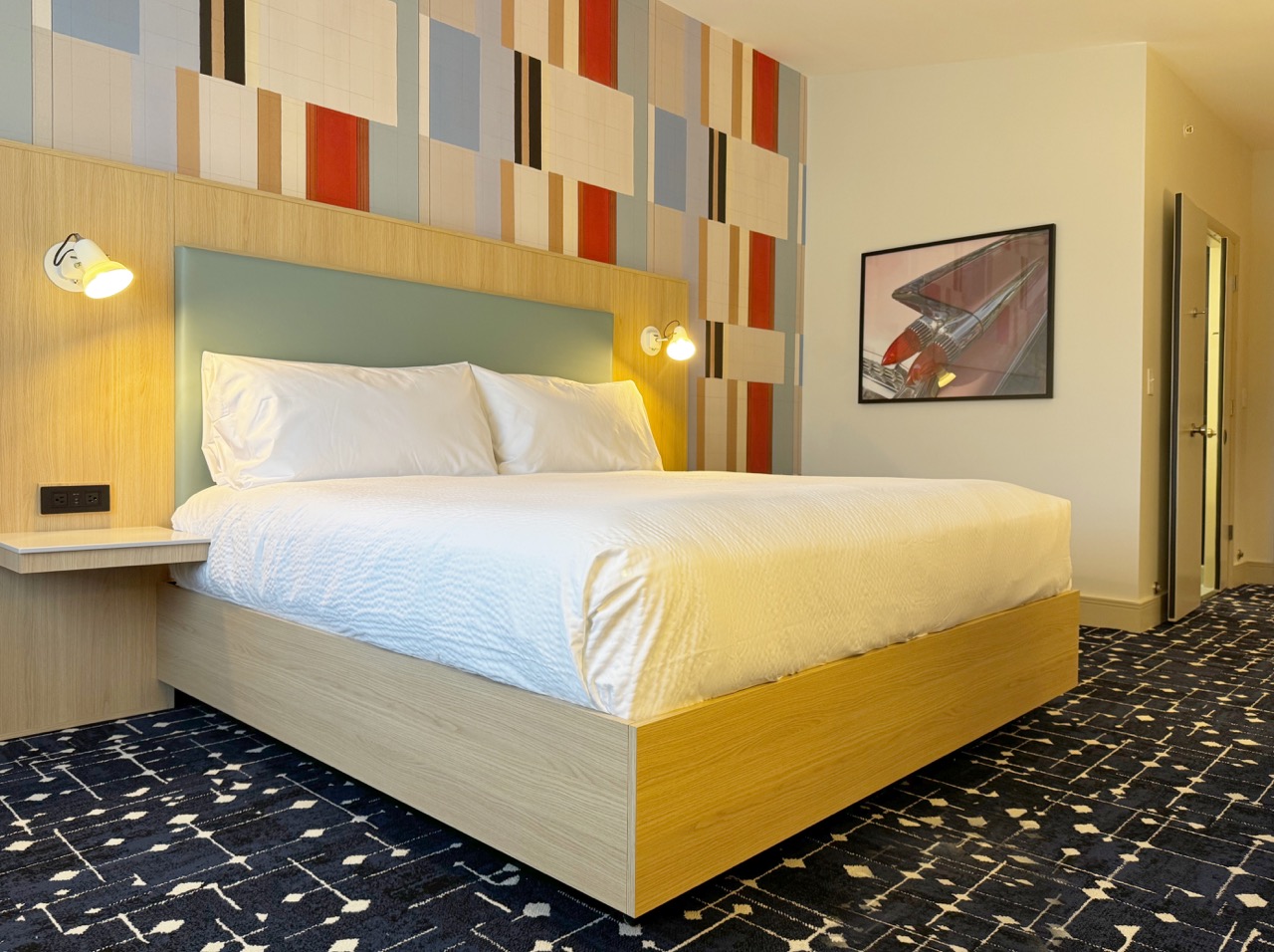 Bed in room with side tables and colorful wall pattern behind headboard
