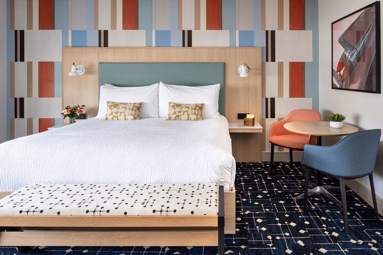 Hotel bed and night stand with colorful patterned wall behind the head of the bed