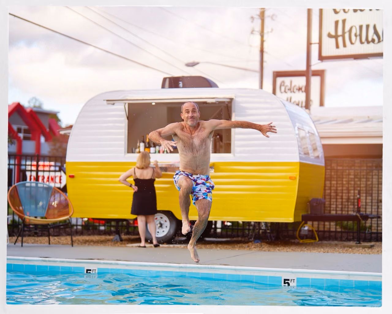 hotel guest jumping into outdoor pool with colorful concession trailer in the background