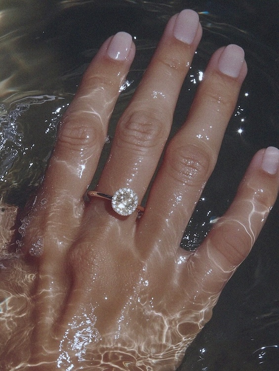 Close-up of a hand with a sparkling oval-cut diamond engagement ring submerged in shimmering water.