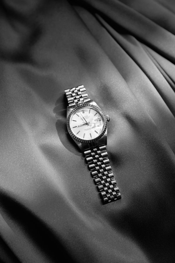 A black and white image of a Rolex Oyster Perpetual watch laying on satin fabric.