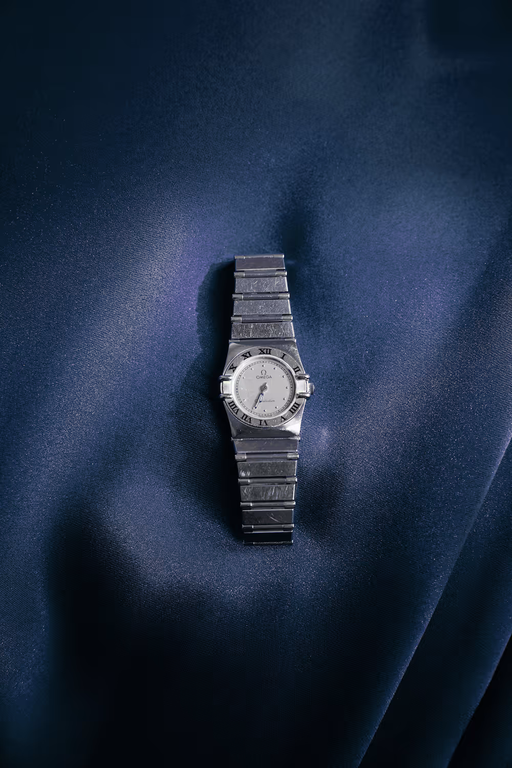 Silver and gold OMEGA Constellation watch on blue satin fabric.