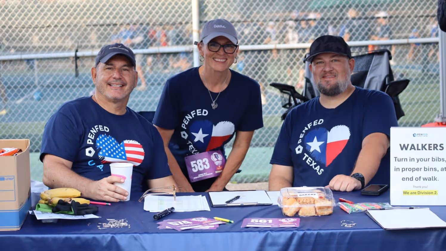 Group of three PenFed workers volunteering at a community event standing at their organization's table