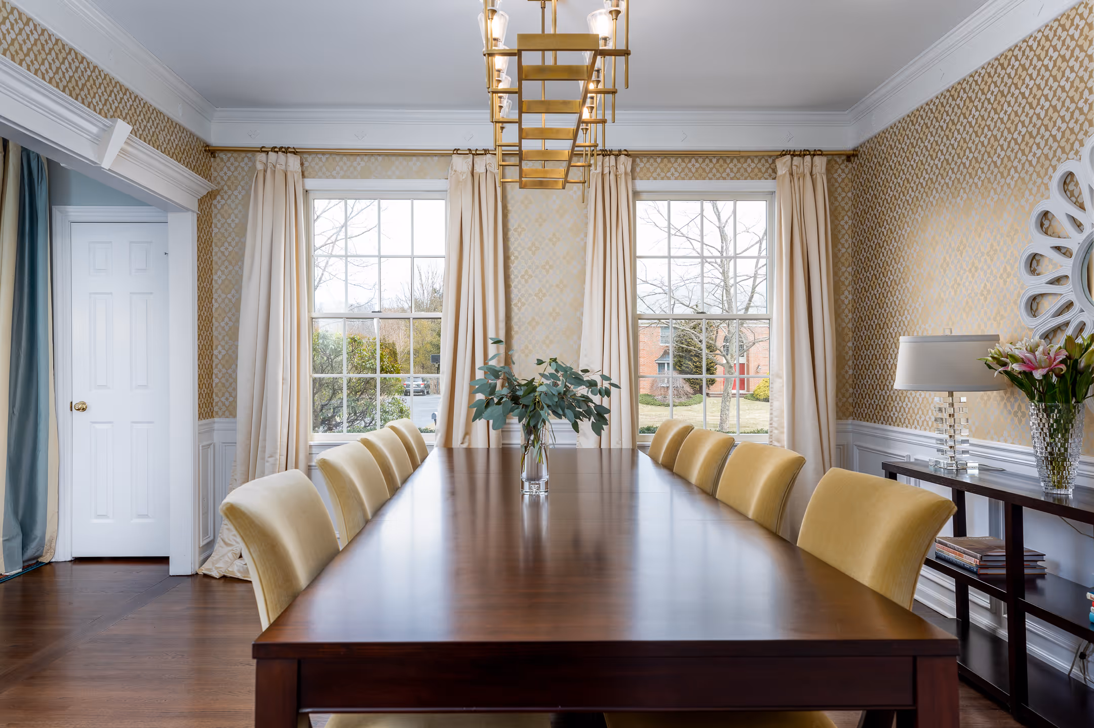 A beautiful symetrical image of a dining room with 2 outside windows in the background.