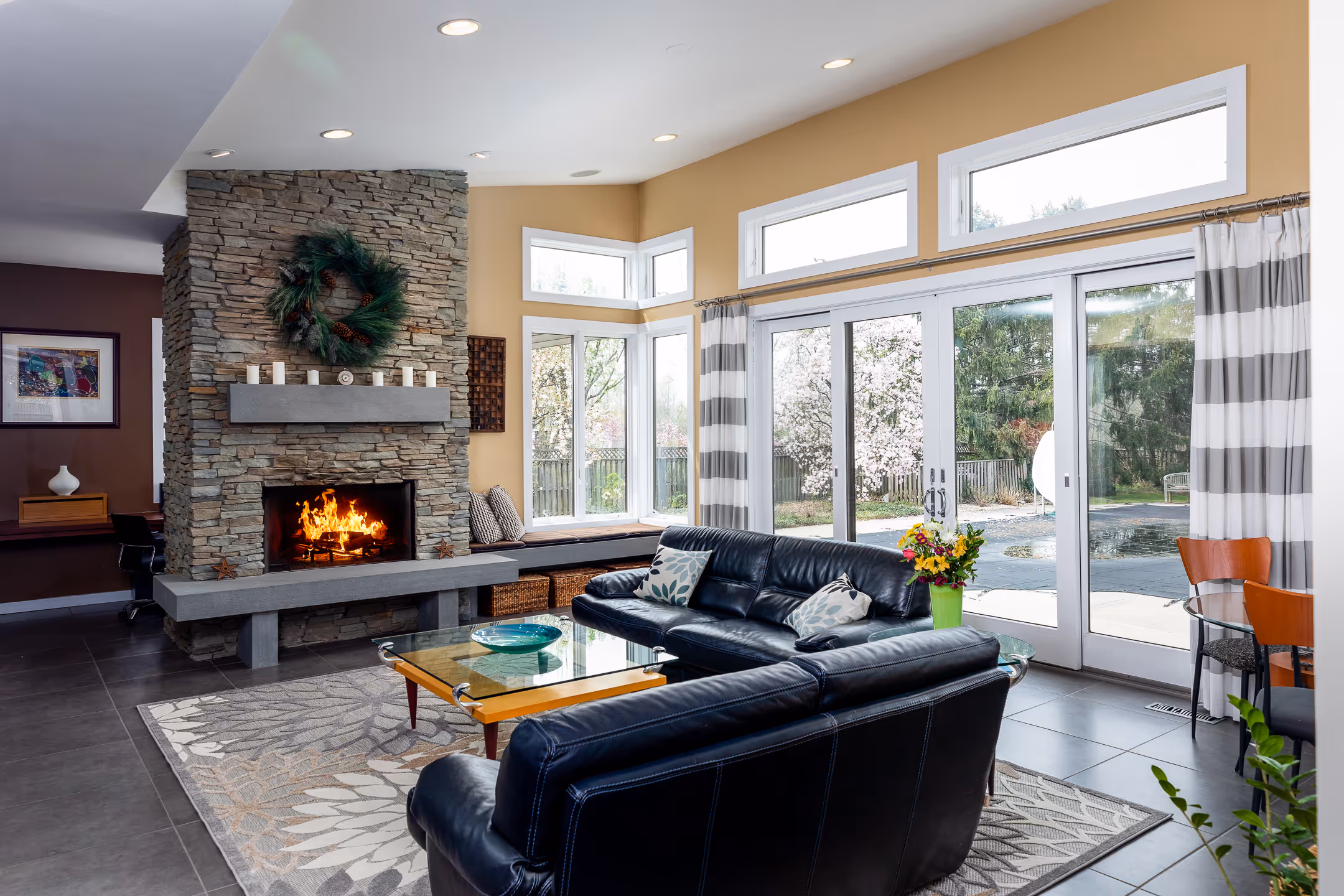 A real estate image of a living room with a roaring fire place over looking the backyard through slider patio doors.