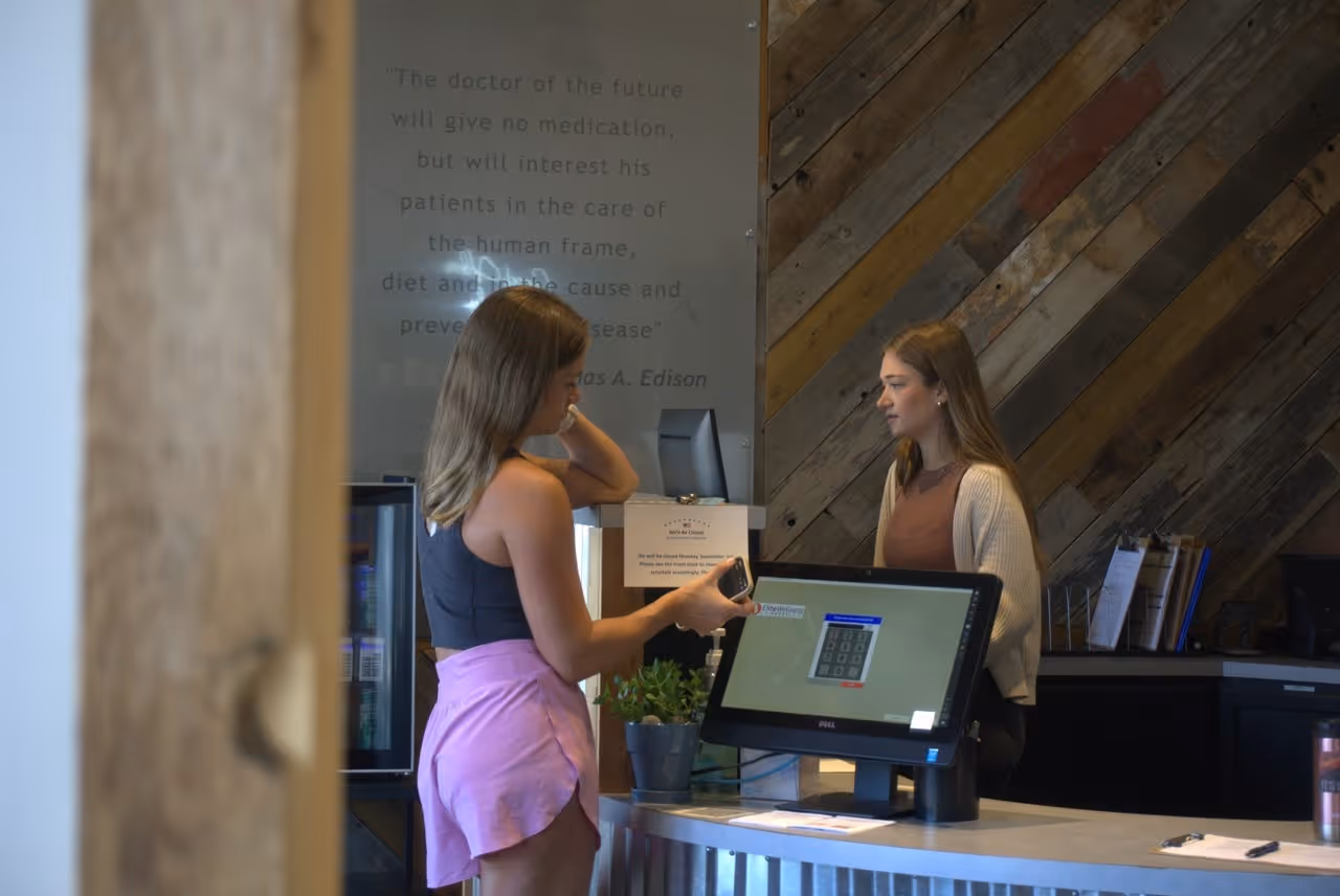 Patient checking out at the front desk of a chiropractic clinic after an appointment while speaking with a team member about follow-up care, scheduling, or treatment plans.