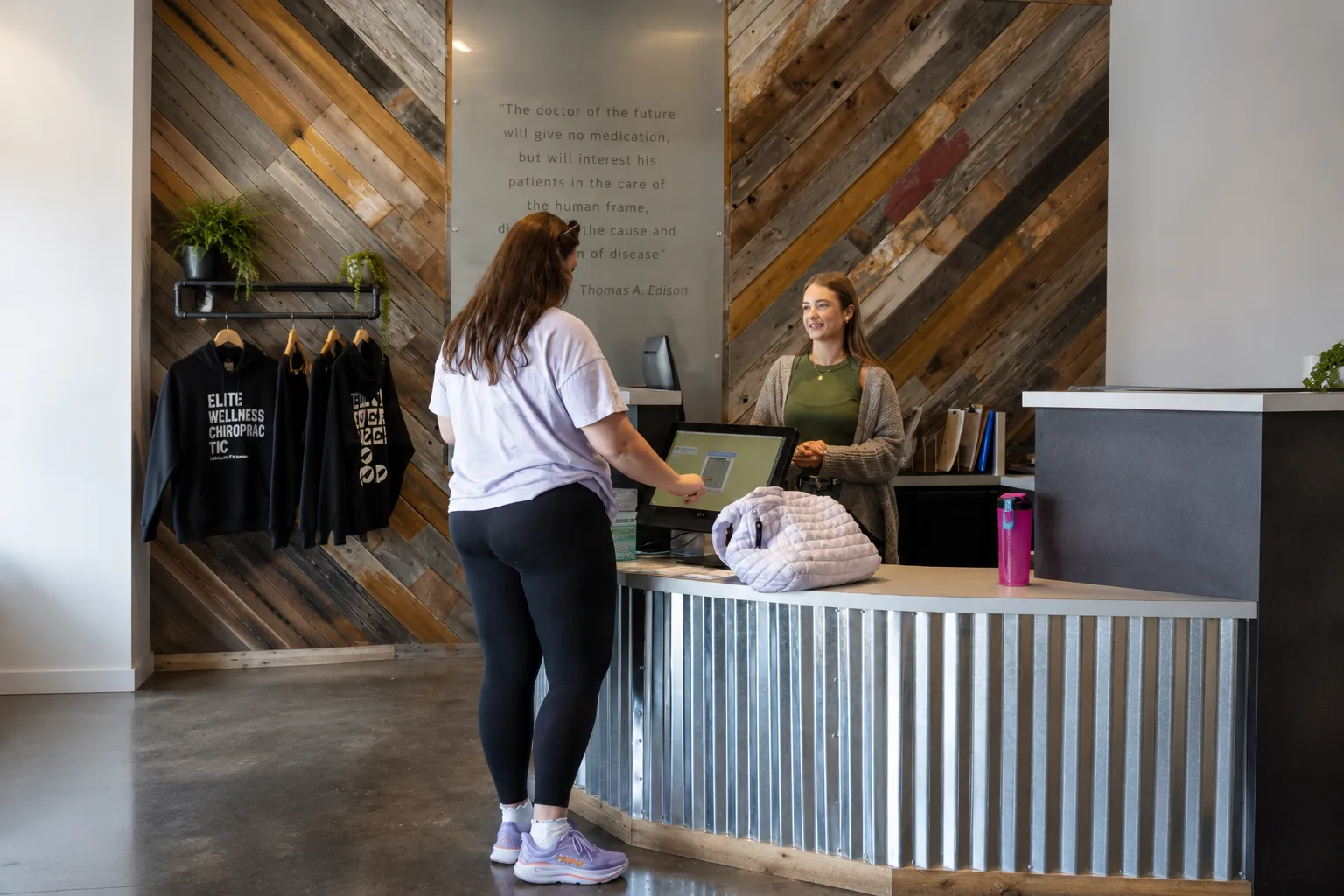 Patient checking in at the Elite Wellness Chiropractic reception desk while speaking with a receptionist in a modern chiropractic clinic.