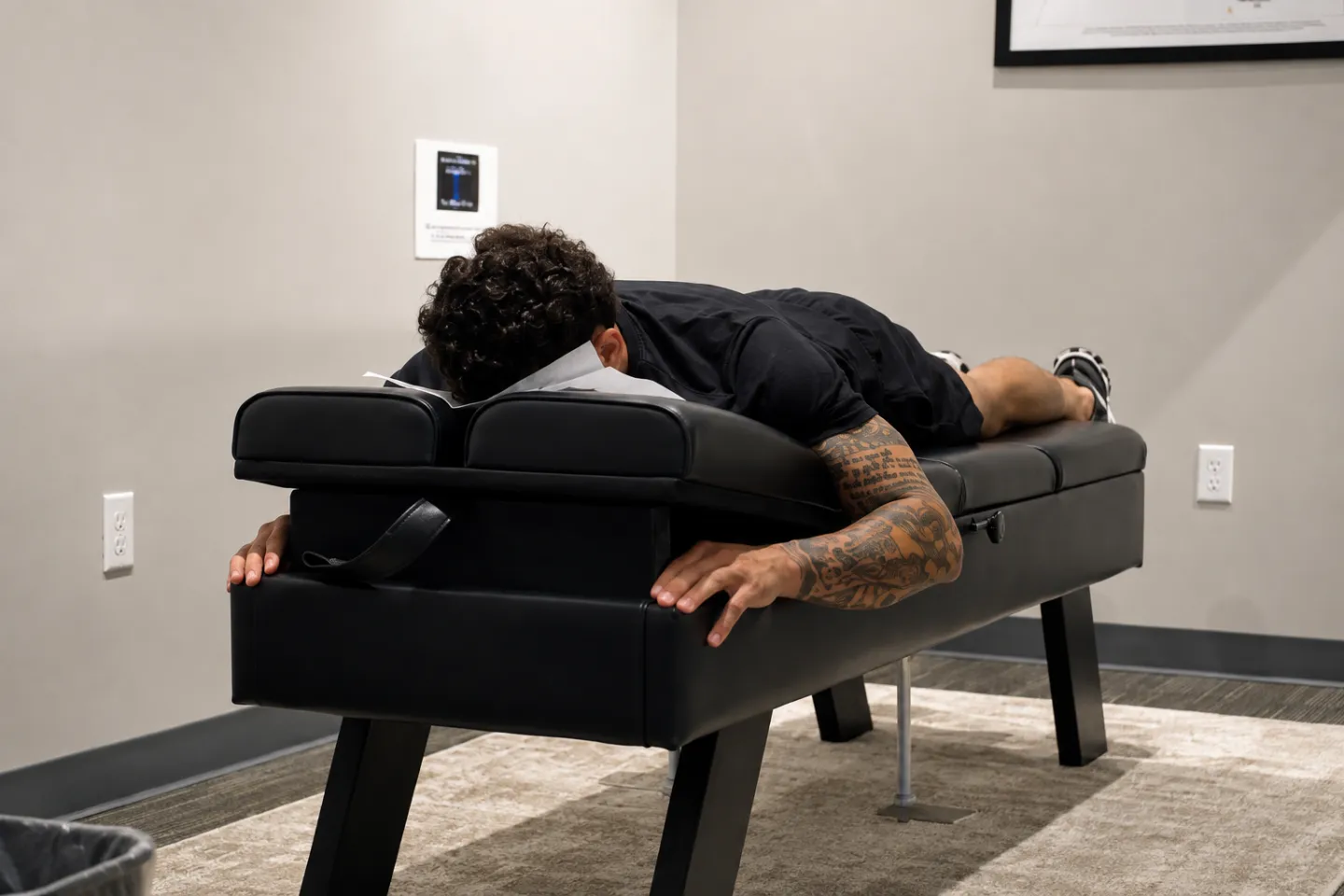 A male patient lies face down on a chiropractic treatment table during a visit at a modern chiropractic clinic.