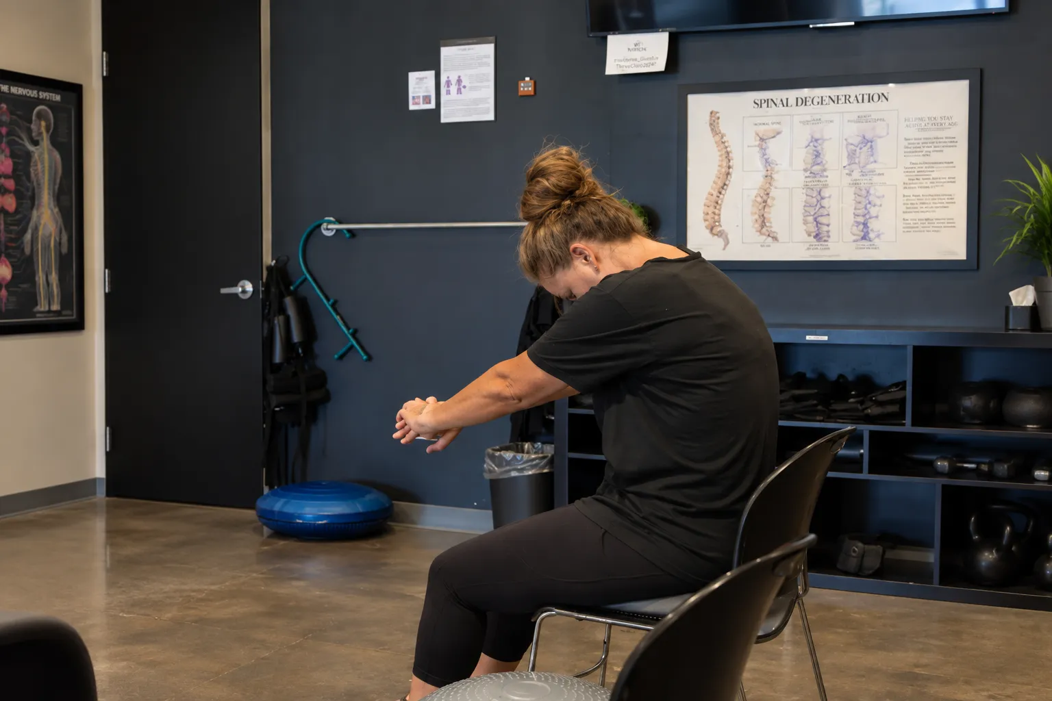 Woman seated at Elite Wellness Chiropractic performing a forward stretch with her head and arms lowered.
