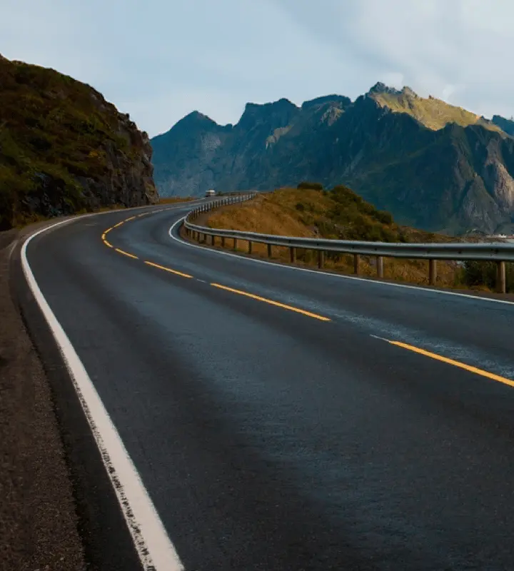 Carretera asfaltada con líneas amarillas y blancas curvándose junto a montañas rocosas.