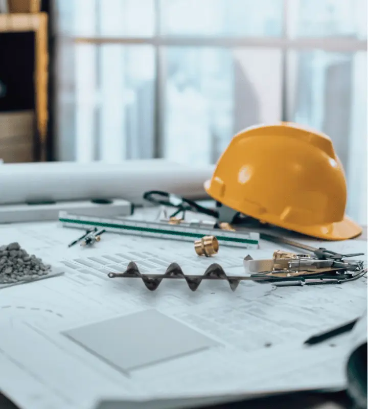 Casco amarillo y herramientas sobre planos en mesa de trabajo, ambiente de construcción e ingeniería.