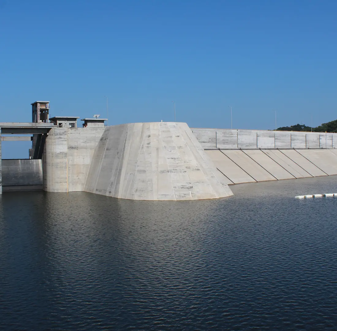 Estructura de presa de concreto con agua represada bajo cielo azul despejado.