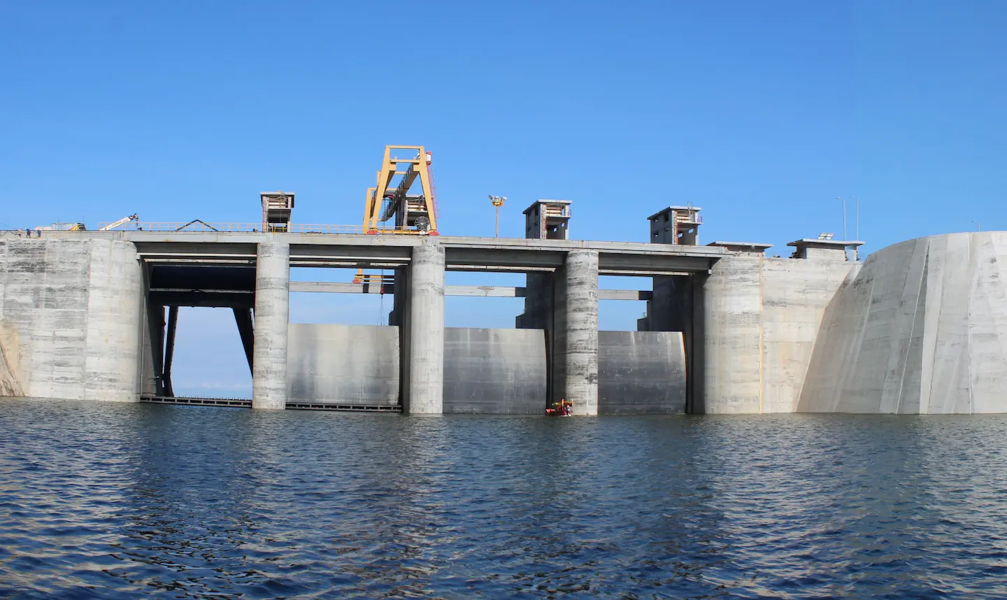 Gran presa de concreto con pilares y estructuras en un embalse bajo cielo azul.