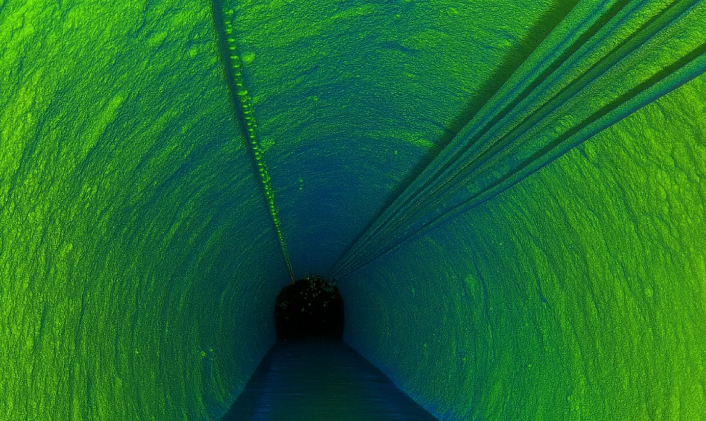 Imagen de un túnel escaneado en 3D con colores verde y azul mostrando textura y cables internos.