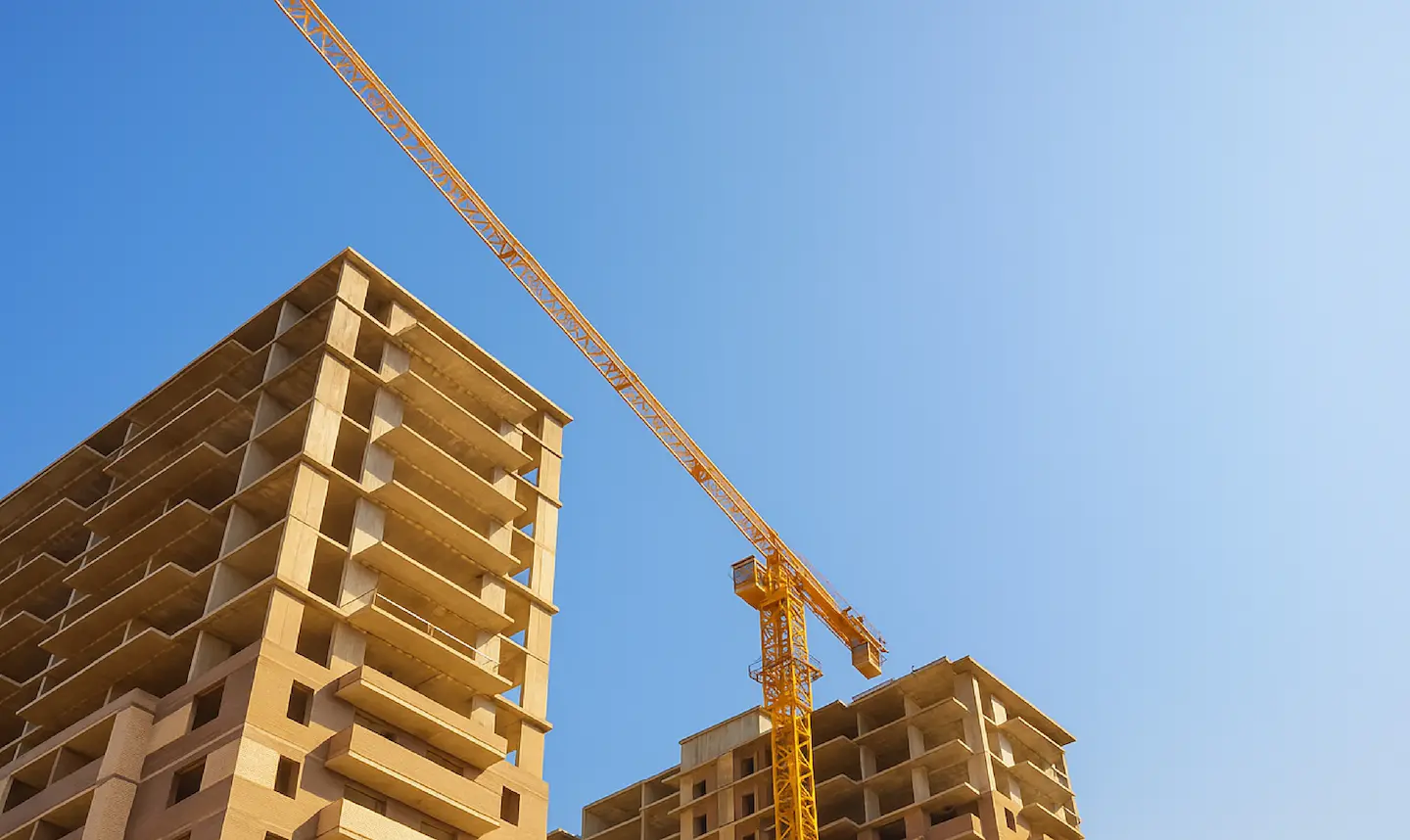 Grúa amarilla sobre edificios en construcción bajo un cielo despejado y azul.