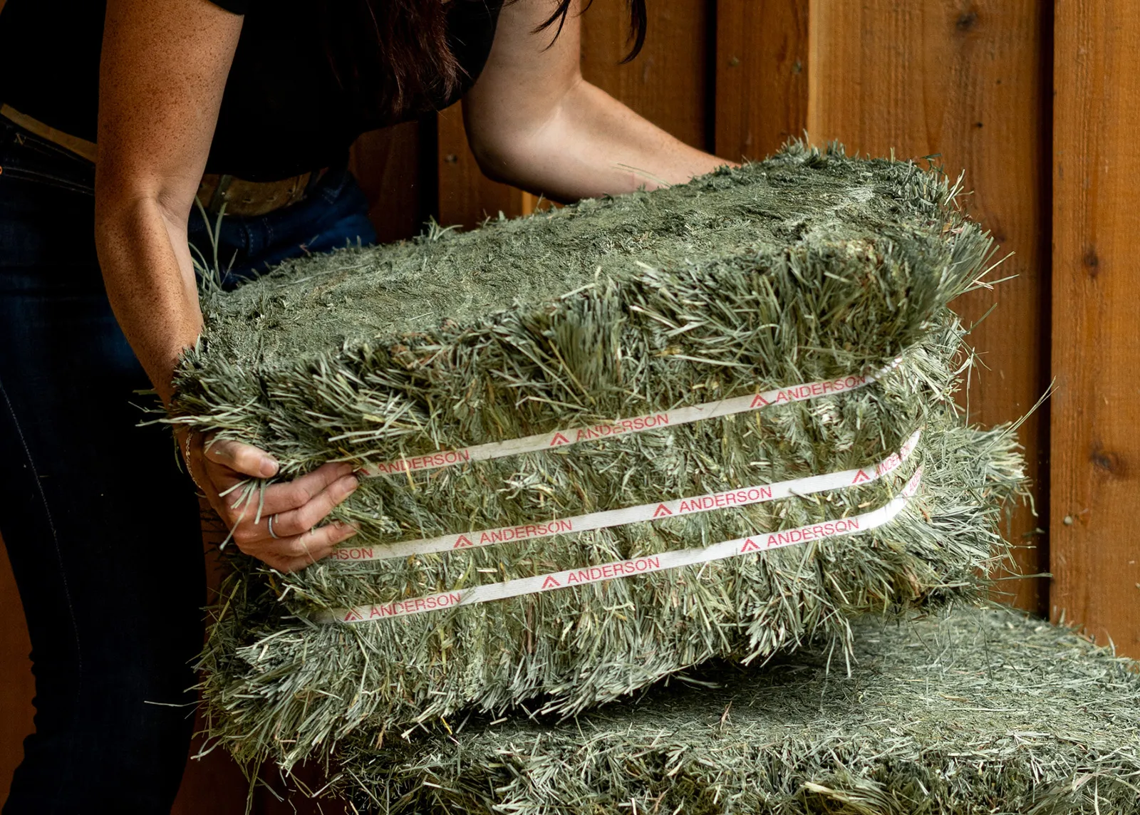 A woman picking up a compressed bale of Anderson Hay