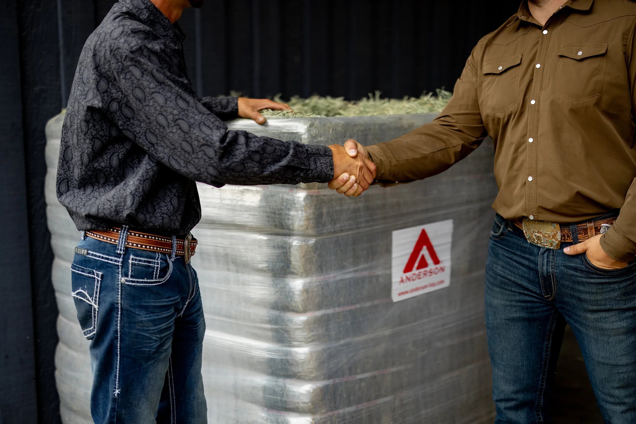 2 men shaking hands in front of a MAG bale of Anderson hay 