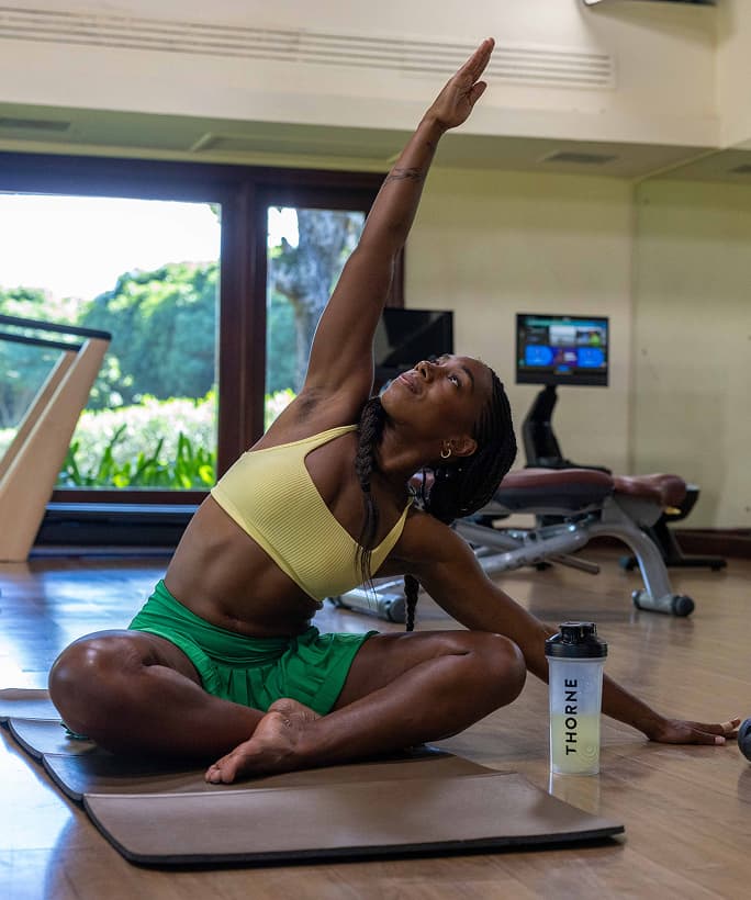 Trainer Games contestant Divinity Gaines doing a seated side stretch with a Thorne shaker bottle beside her