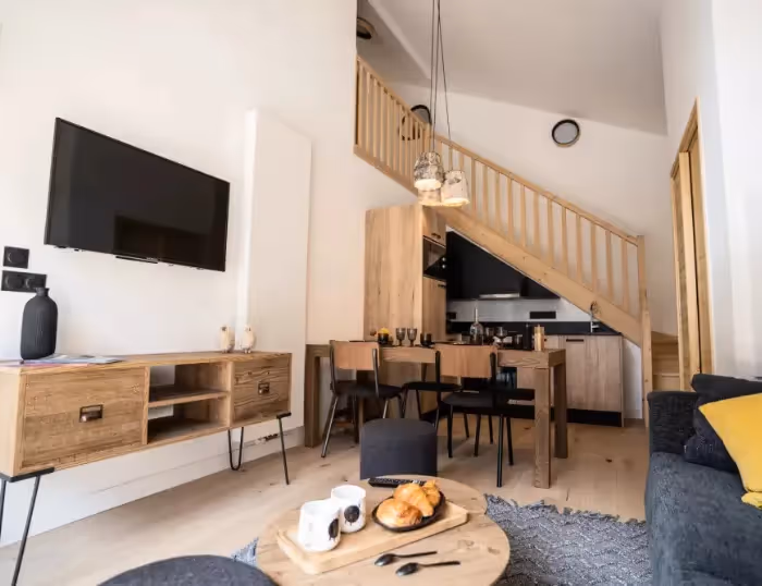 Séjour lumineux dans un appartement de vacances à Combloux, Haute-Savoie, avec table à manger, escalier en bois et vue sur le Mont-Blanc.