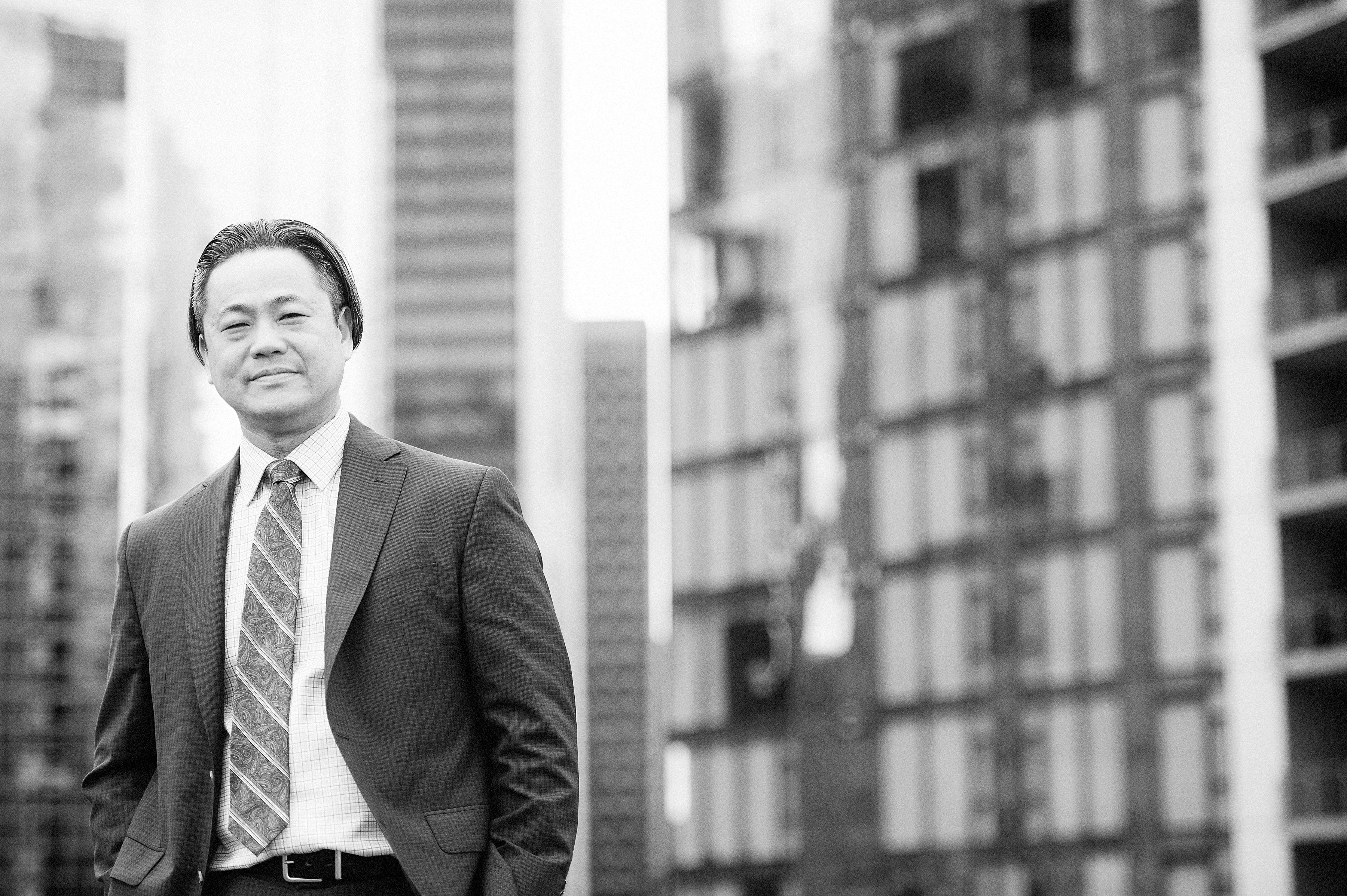 Man smiling with blurred photo of downtown building behind him.