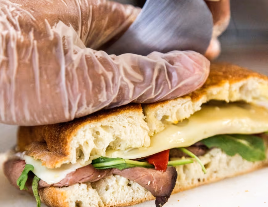 Image of a deli sandwich being cut down the middle. 