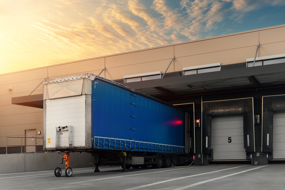 Blue freight trailer backed into a loading dock at a modern warehouse during sunrise, highlighting Element Trailers’ commitment to efficient logistics and delivery.