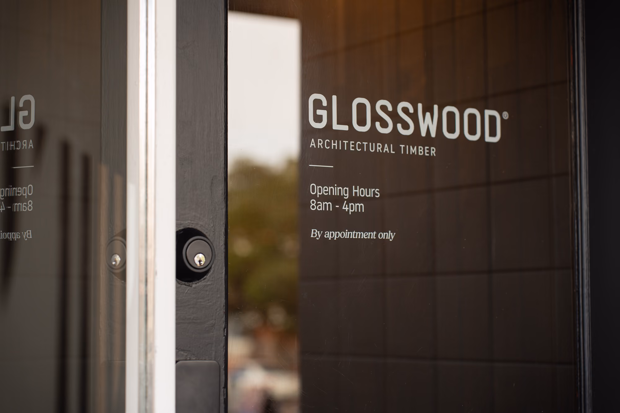 Glass door with Glosswood Architectural Timber logo and opening hours 8am to 4pm by appointment only.