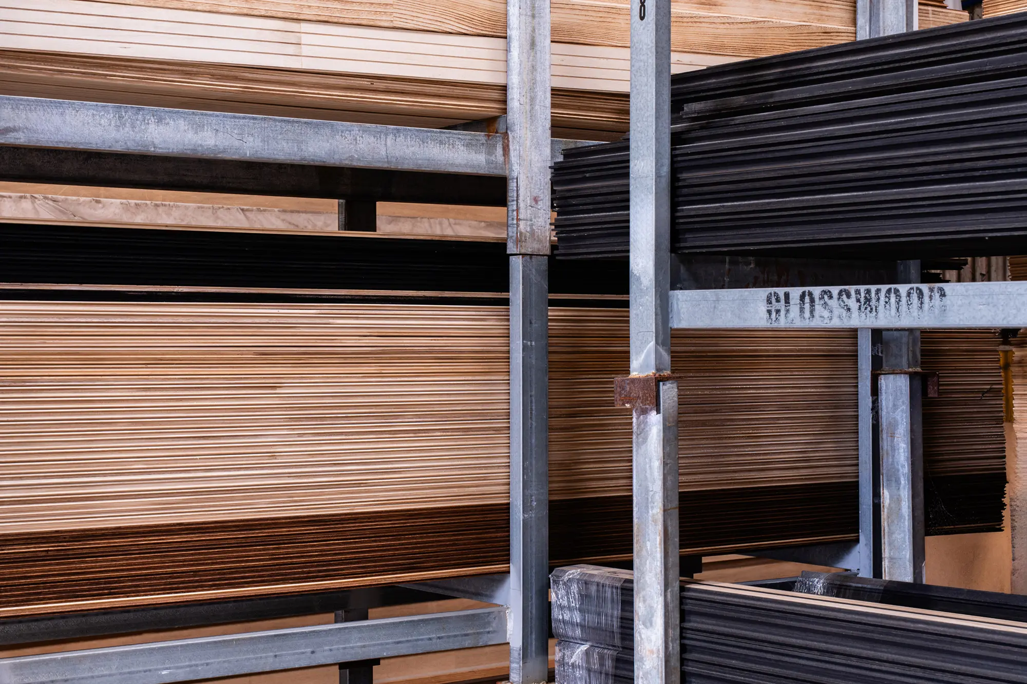 Stacks of layered wooden planks held in metal racks in a warehouse.