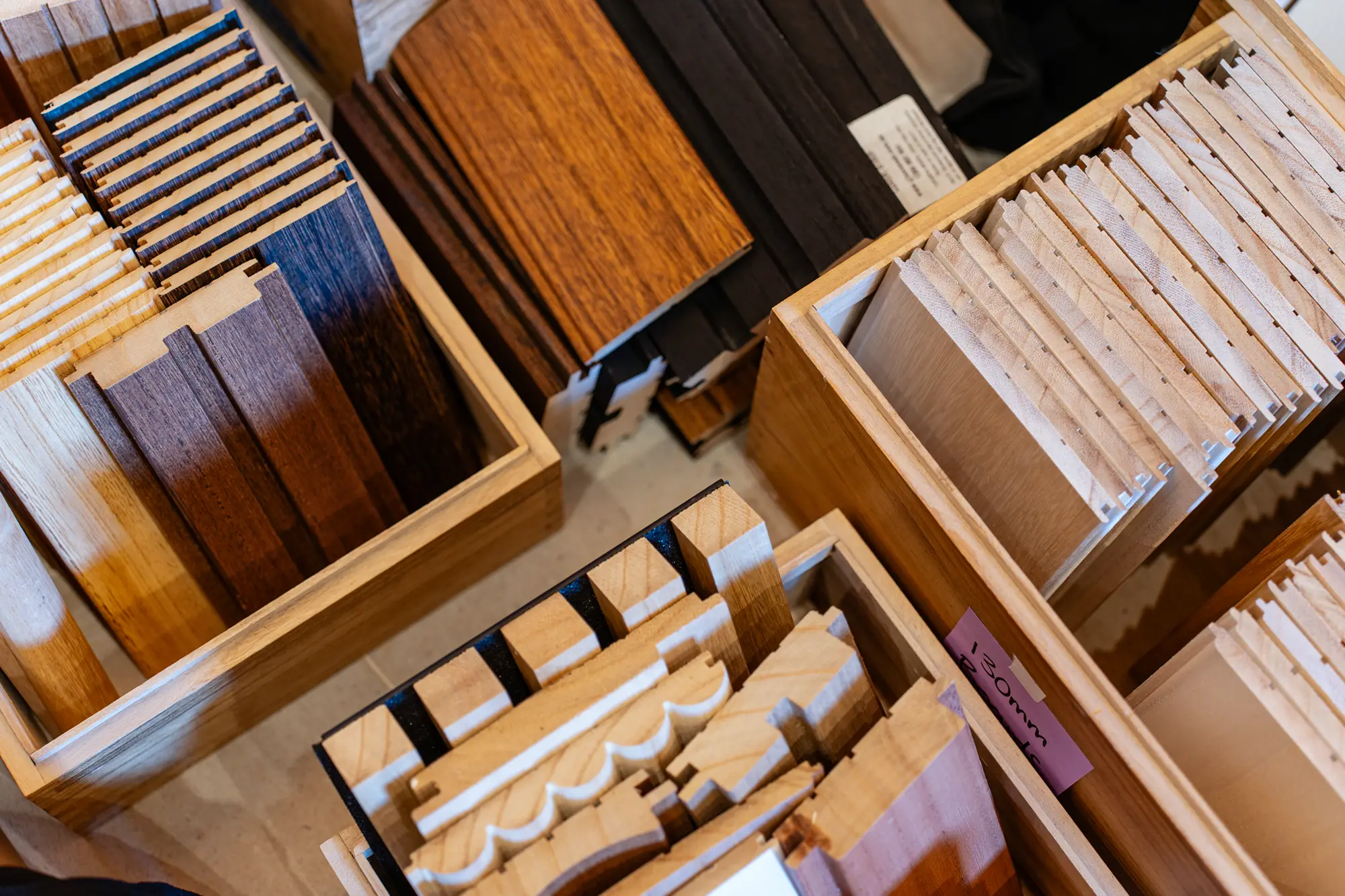 Wood samples organized by color and type in wooden boxes, including planks and intricate molding pieces.