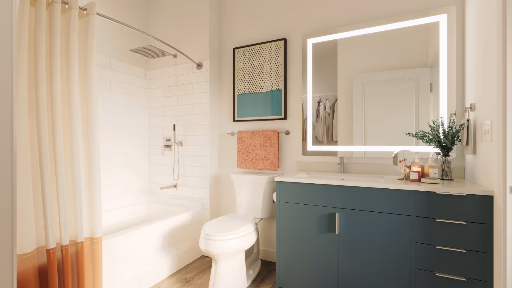 Modern bathroom with a blue vanity, an illuminated mirror, and a full-size bathtub/shower, in an apartment at The Rook in Orlando, FL.