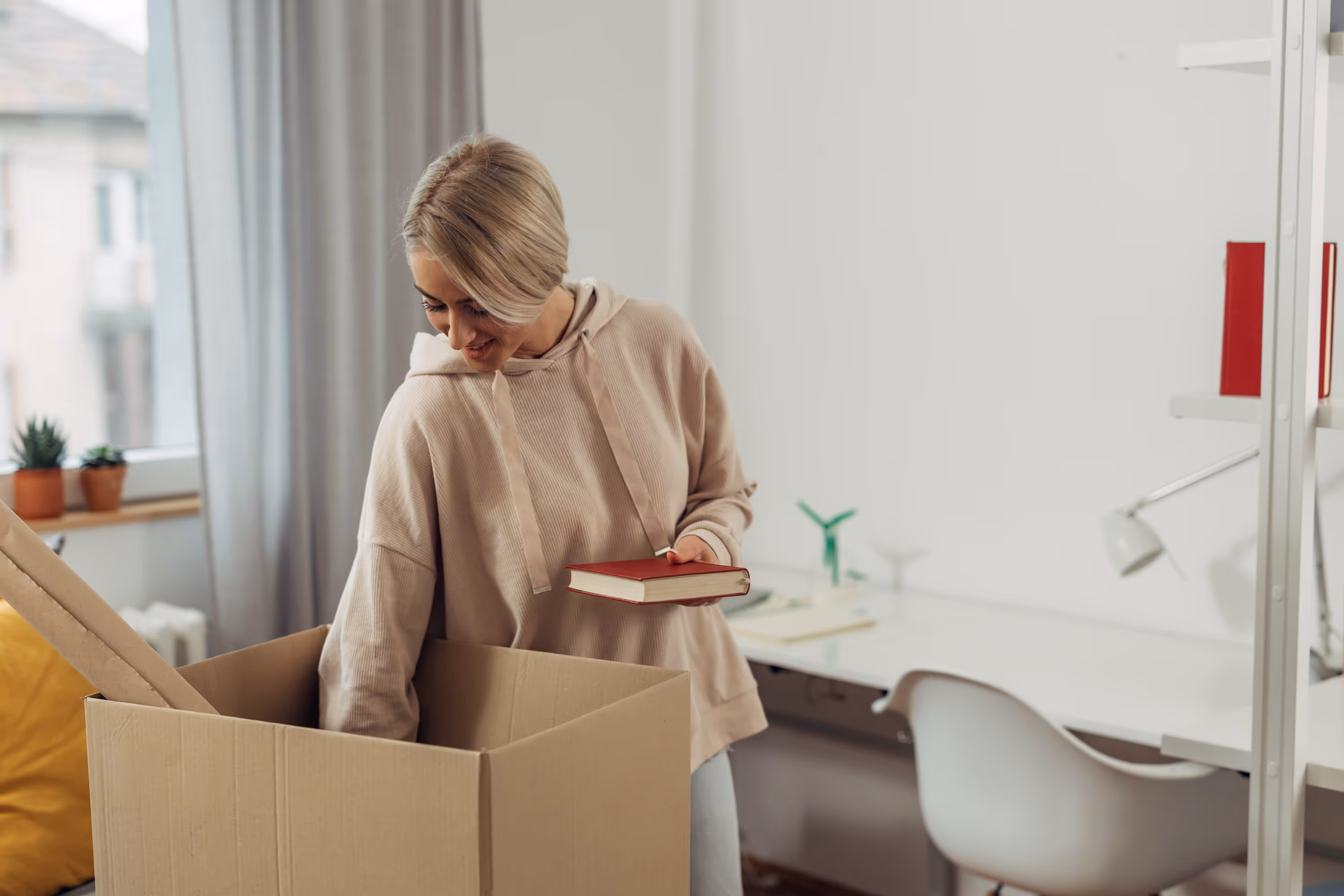A female student smiling while unpacking a book from a moving box in her bright, newly moved-in apartment, representing the seamless move-in process at The Rook in Orlando, FL