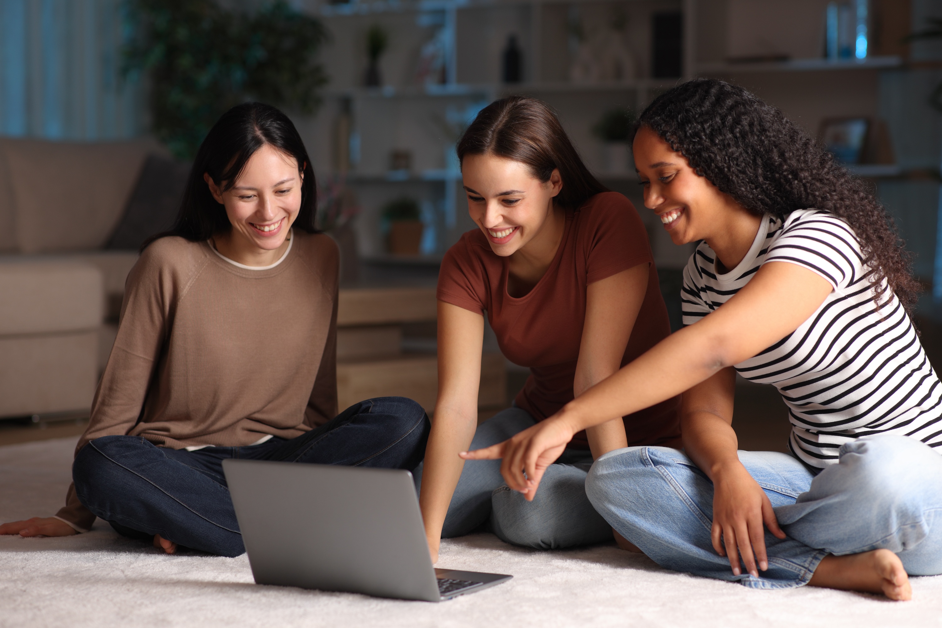 Residents at The Rook apartments gathering in a spacious living area to share a laptop screen, highlighting the community's comfortable atmosphere.
