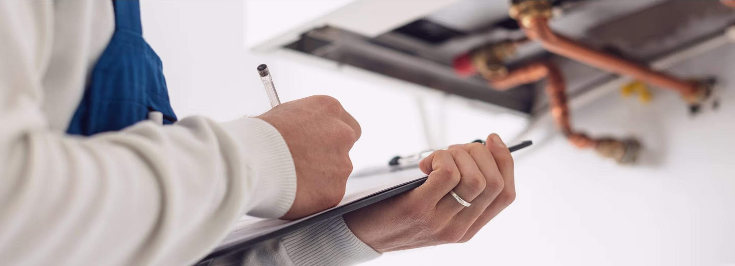 Mitarbeiter notiert sich Informationen auf einem Klemmbrett. Im Hintergrund Heizungsanlage