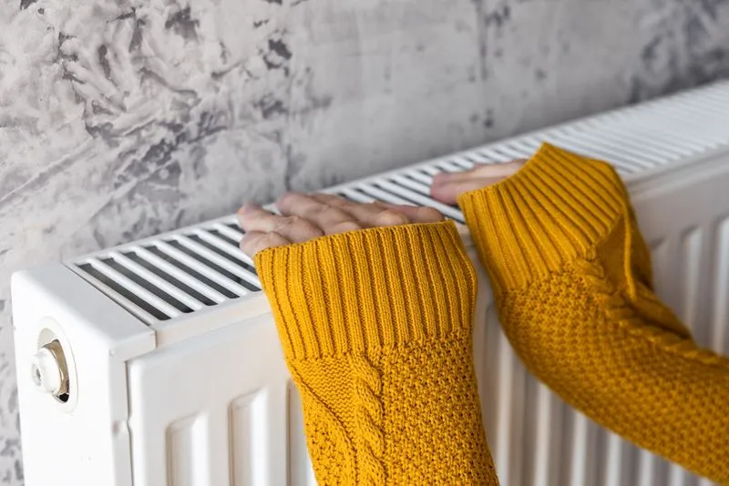 Frau mit gelbem Pulli wärmt ihre Hände an einer Wärme360° Heizung