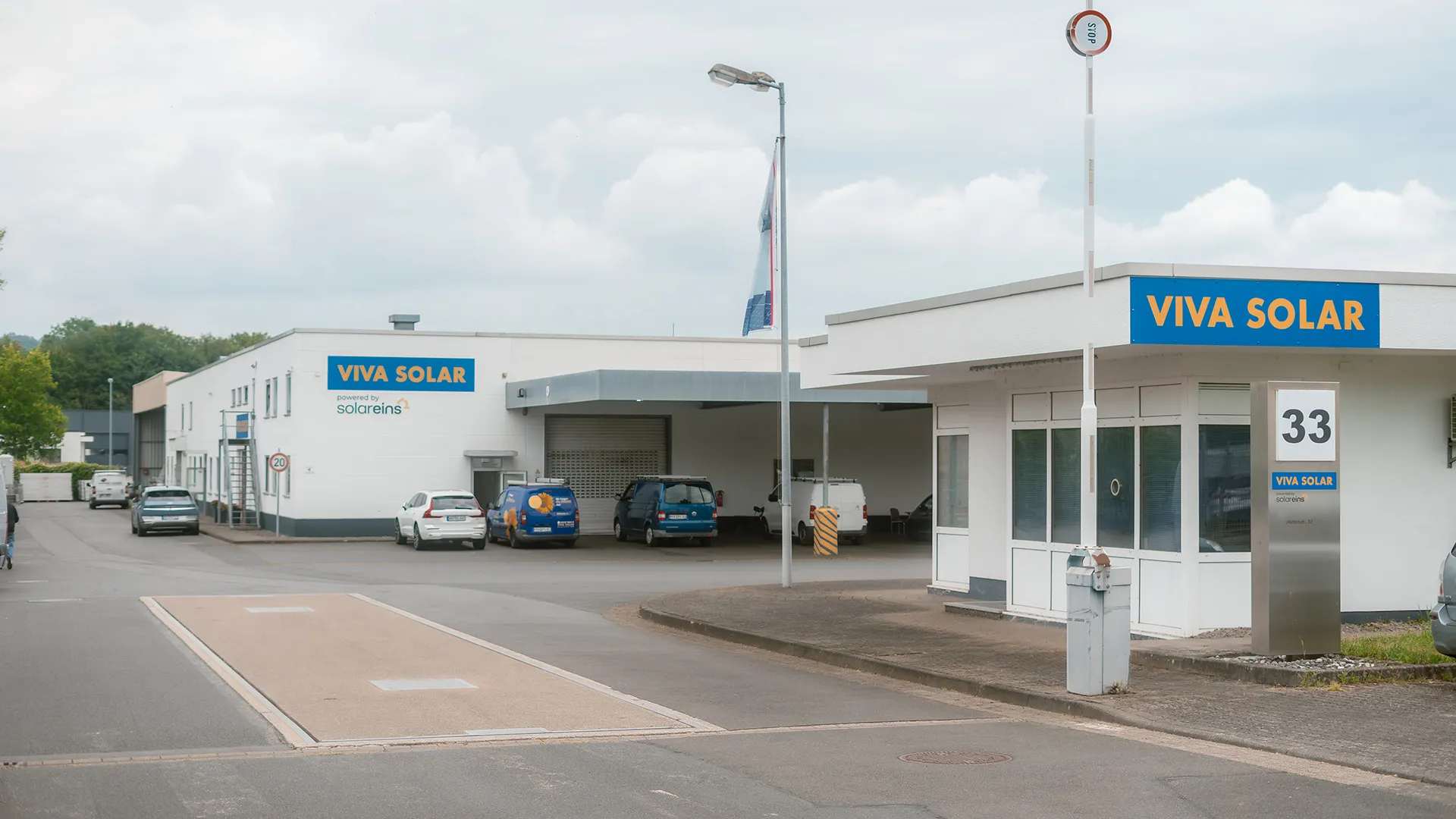 Building facade with "VIVA SOLAR" sign. Vehicles parked outside, including a blue van. Cloudy sky in background.