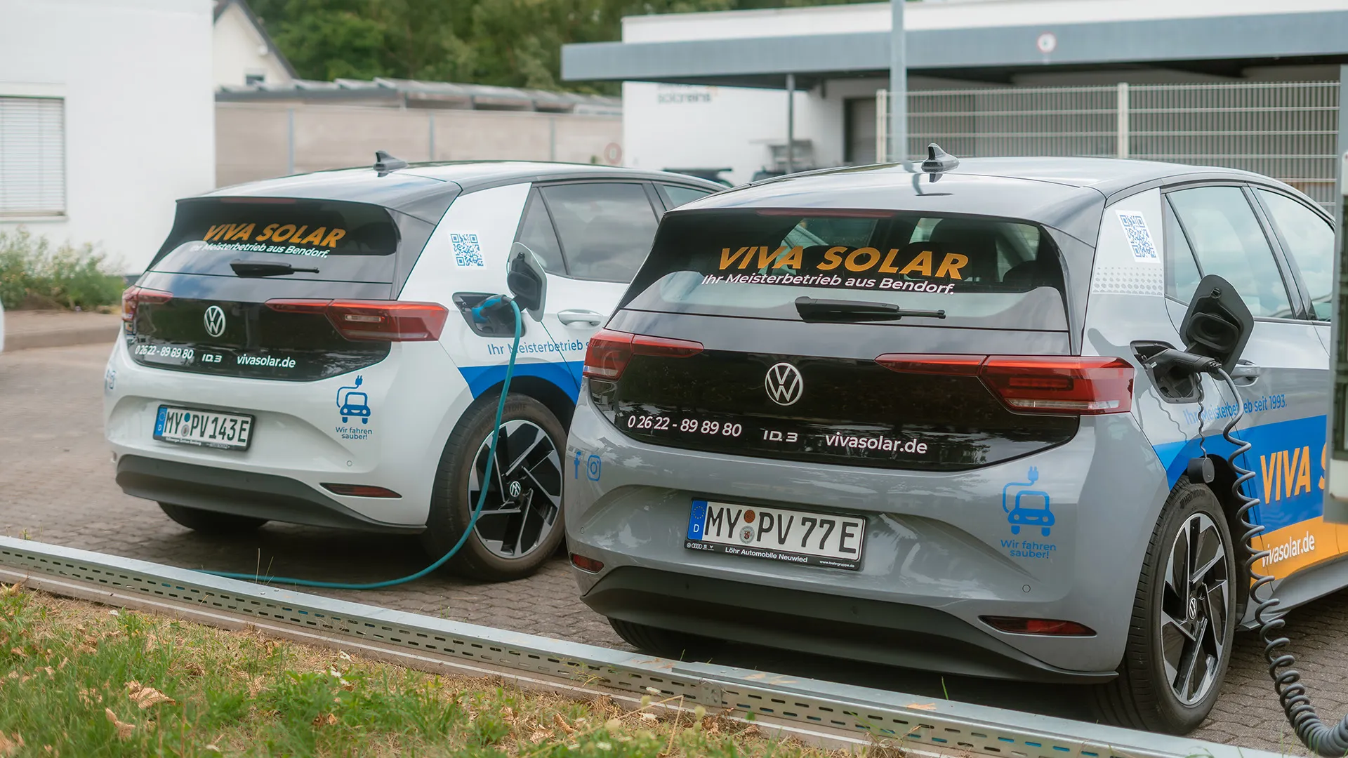 Zwei Elektroautos der Marke Volkswagen mit dem Schriftzug „VIVA SOLAR“ werden aufgeladen. An einem Auto ist ein Ladekabel angeschlossen.