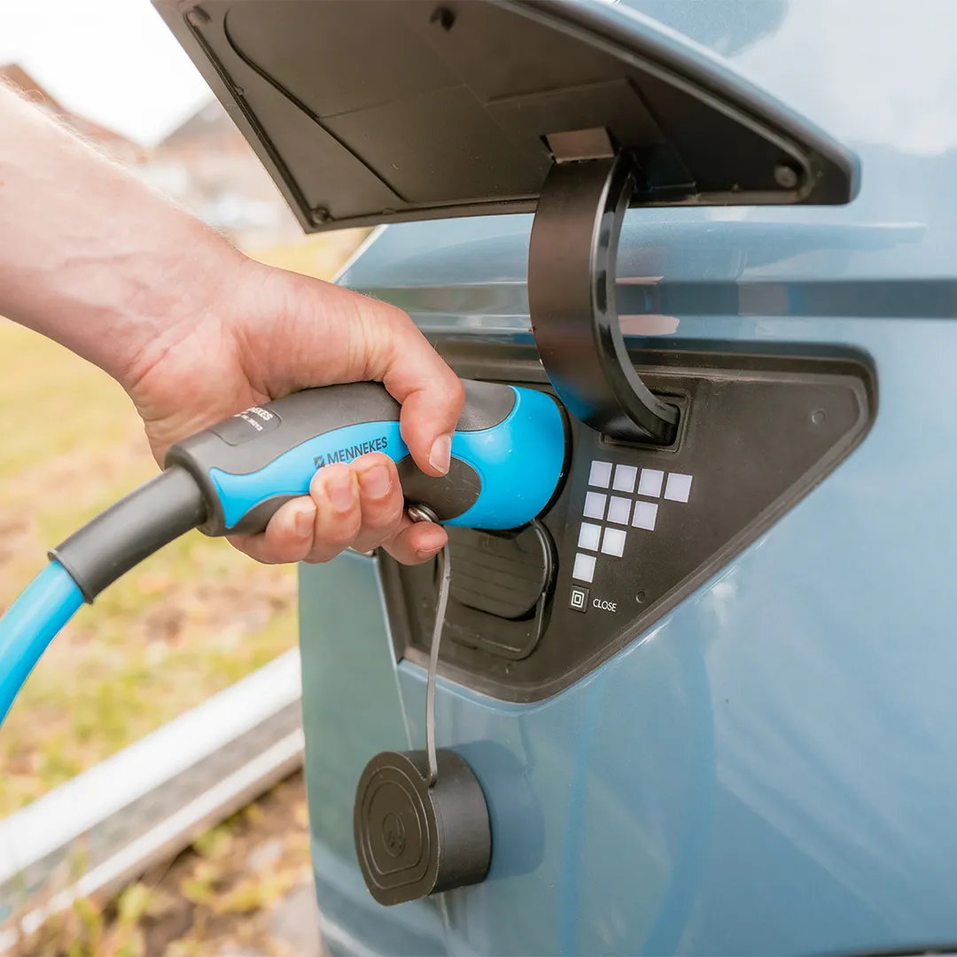 Eine Hand verbindet einen blau-schwarzen Ladestecker mit dem Ladeanschluss eines Elektrofahrzeugs und zeigt dabei Tasten und eine Schließfunktion.