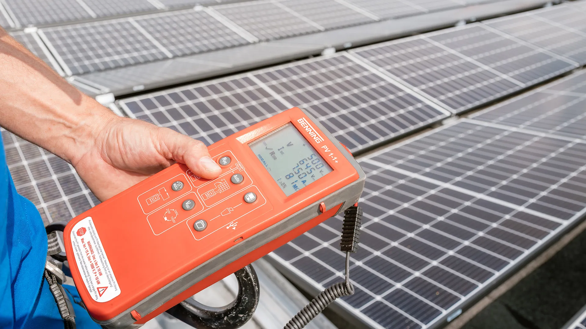 Eine Person hält einen Solarpanel-Tester über mehrere Solarpanels und zeigt die Messwerte auf dem Bildschirm an.
