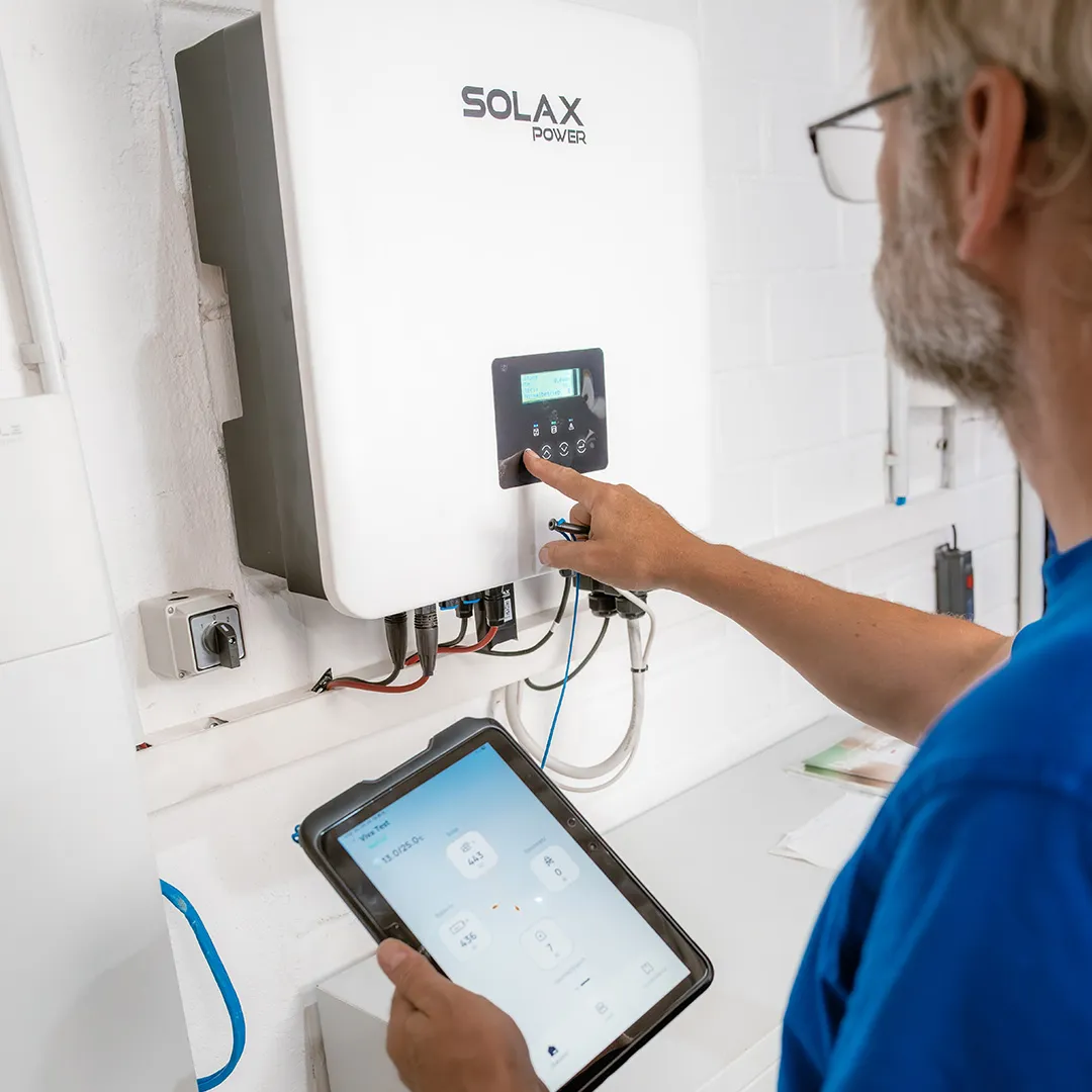 Eine Person stellt einen SOLAX Power-Wechselrichter über ein Touchscreen-Tablet ein und zeigt dabei die Überwachung der Solarenergie in einer technischen Anlage.
