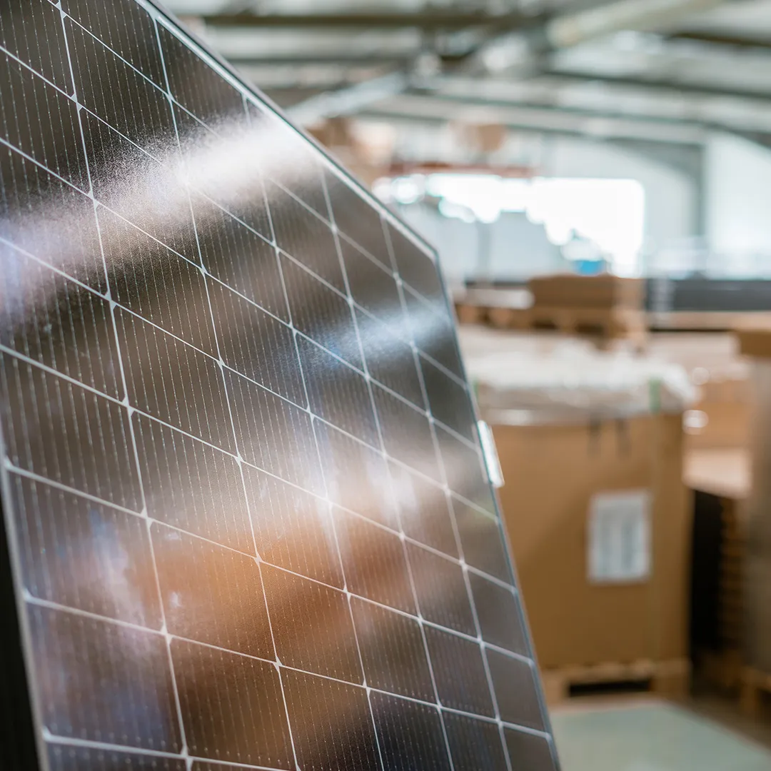 Nahaufnahme eines Solarpanels mit reflektierendem Glas vor einem unscharfen Hintergrund aus Kisten in einem Lagerhaus.