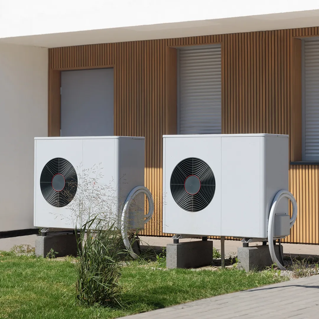 Zwei Wärmepumpen mit großen Ventilatoren sind neben einem modernen Gebäude aufgestellt, vor dem sich eine Rasenfläche befindet.