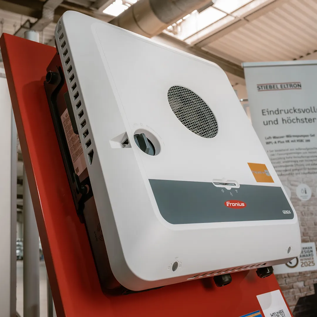 Ein Fronius-Gerät, montiert auf einem roten Display, mit Lüftungsöffnungen und Bedienelementen, in einer hellen, industriellen Umgebung.