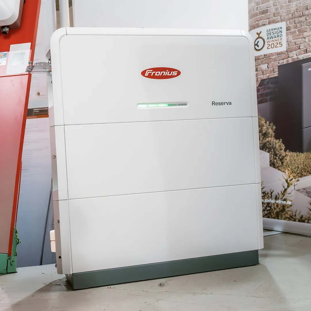 Ein weißer Energiespeicher mit der Aufschrift „Fronius Reserva” und einer grünen Kontrollleuchte, der in der Nähe eines Werbedisplays aufgestellt ist.