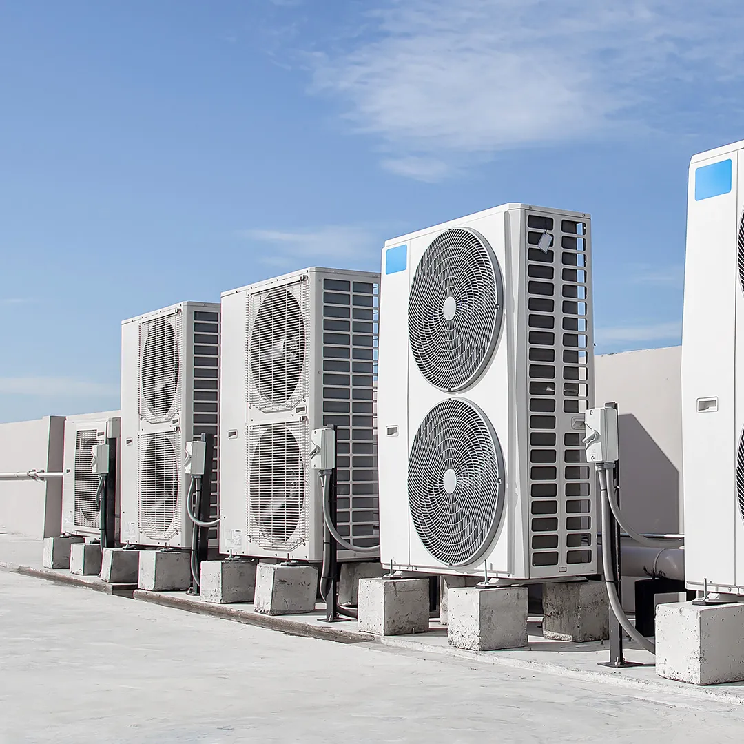 Vier große Wärmepumpen auf einem Dach, mit strahlend blauem Himmel im Hintergrund.